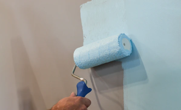 Personne appliquant une peinture blanche sur un mur intérieur gris à l'aide d'un rouleau à peinture